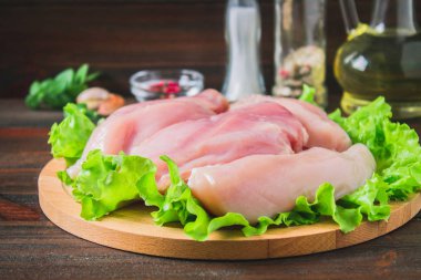 Ahşap masa arka plan üzerinde yuvarlak kesme tahtası üzerinde çiğ tavuk fileto ve yeşil salatası. Yemek pişirmek için et malzemeler.