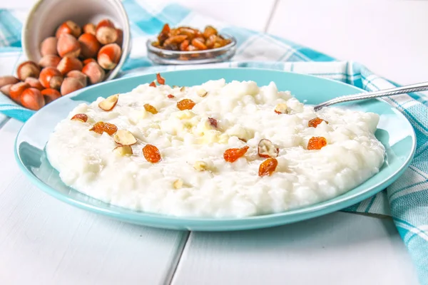 Porridge di latte di riso con noci e uva passa in un piatto blu su un tavolo di legno bianco . — Foto Stock