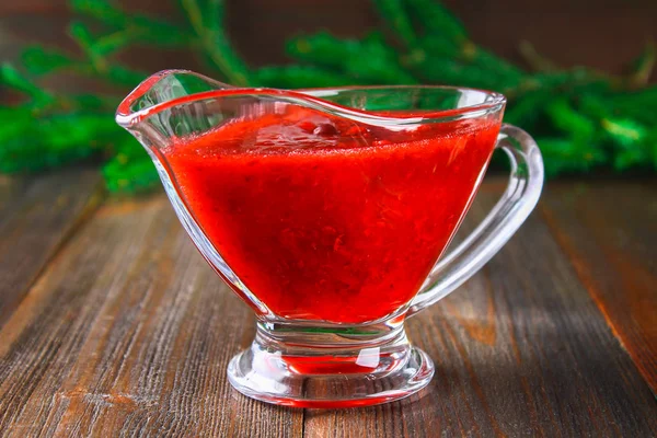 Salsa de arándano de fresa en un platillo transparente de vidrio sobre una mesa de madera con ramas de abeto . — Foto de Stock