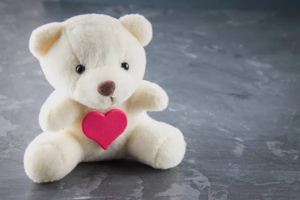 White toy teddy bear with heart on a gray background. The symbol — Stock Photo, Image