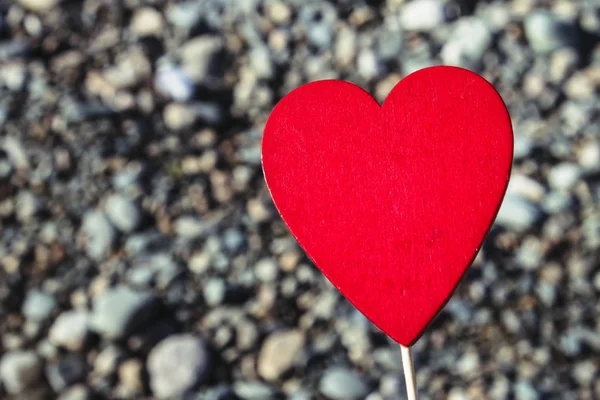 En man innehar ett rött trä hjärta på en pinne mot bakgrund av natur, sky, stenar. Begreppet alla hjärtans dag. — Stockfoto