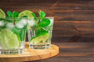 Mojito nane ve limon bir cam ve yuvarlak tahta üzerinde bir sürahi ile. Kahverengi ahşap zemin