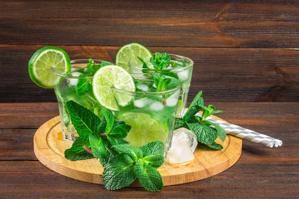 Mojito com hortelã e limão em um copo e um jarro na tábua redonda. Fundo de madeira marrom — Fotografia de Stock