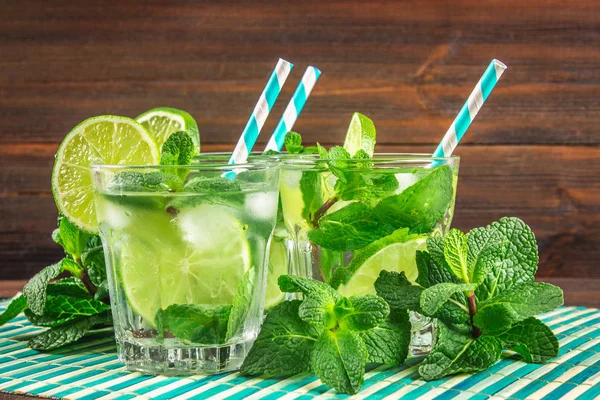 Mojito con menta y lima en un vaso y una jarra en la mesa redonda. Fondo de madera marrón —  Fotos de Stock