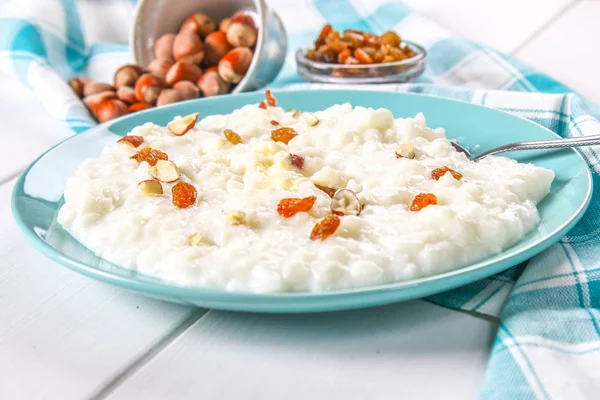 Porridge di latte di riso con noci e uva passa in un piatto blu su un tavolo di legno bianco . — Foto Stock