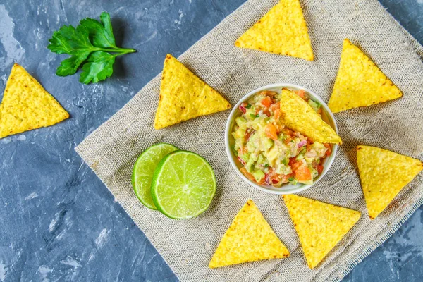 Guacomole is een traditionele Mexicaanse saus uit geraspte avocado, limoensap, rode ui, tomaten, knoflook en chili. Geserveerd met nachos chips. — Stockfoto