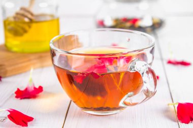 Bir fincan çay, bal ve bir kavanoz siyah bir bitki çiçek çayı ile bir banka beyaz ahşap bir masa üzerinde arka planda.