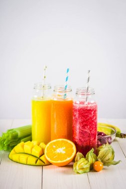 Mango, portakal, muz, kereviz, çilek, ahşap bir masa üzerinde şişelerde çok renkli smoothies.