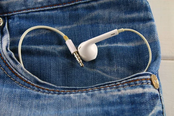Heart of white headphones - a symbol of love peeps out of the pocket of jeans trousers. Love for music. The concept of the day of lovers. St. Valentine's Day. — Stock Photo, Image