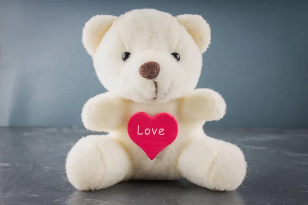 White toy teddy bear with heart on a gray background. The symbol — Stock Photo, Image