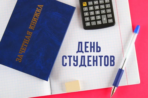 Un libro blu con un'iscrizione in russo - libro di registrazione di uno studente. Penna, calcolatrice e quaderni bianchi su sfondo rosa. Iscrizione in russo - Giorno degli studenti . — Foto Stock