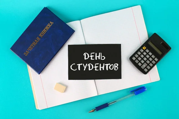 A blue book with an inscription in Russian - a student's record book. Pen, calculator and blank notebooks on a blue background. Inscription in Russian - Students Day. — Stock Photo, Image