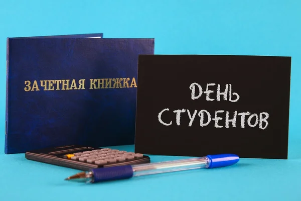 一本带有俄语铭文的蓝色书--学生的记录册。钢笔, 计算器在蓝色背景。俄语学生日题词. — 图库照片
