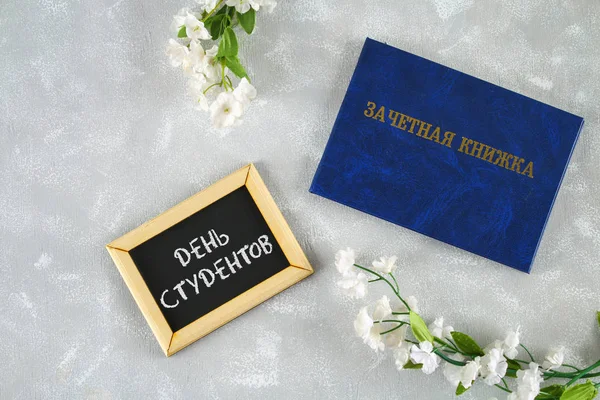 Mavi kitap ile bir yazıt Rusça - bir öğrencinin kayıt defteri. Gri bir arka plan üzerinde beyaz çiçekler. Yazıt Rusça - öğrenciler gün. Tatyana'nın gün. — Stok fotoğraf
