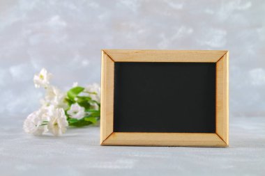 Gri bir arka plan üzerinde beyaz çiçekler çevrili boş bir kutu ile ahşap bir çerçeve içinde Kara tahta. Uzay kopyalayın. Bahar ya da kadın tatil için şablon.