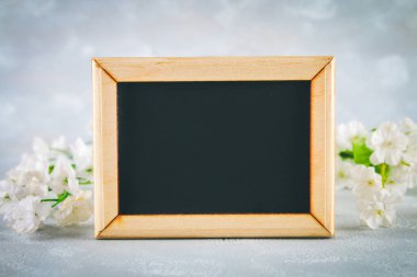 Gri bir arka plan üzerinde beyaz çiçekler çevrili boş bir kutu ile ahşap bir çerçeve içinde Kara tahta. Uzay kopyalayın. Bahar ya da kadın tatil için şablon.