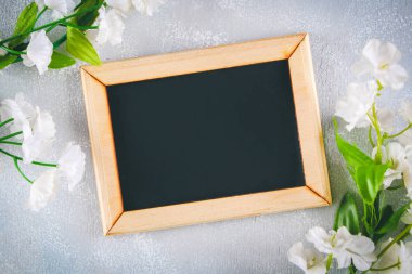 Gri bir arka plan üzerinde beyaz çiçekler çevrili boş bir kutu ile ahşap bir çerçeve içinde Kara tahta. Uzay kopyalayın. Bahar ya da kadın tatil için şablon.