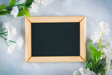Gri bir arka plan üzerinde beyaz çiçekler çevrili boş bir kutu ile ahşap bir çerçeve içinde Kara tahta. Uzay kopyalayın. Bahar ya da kadın tatil için şablon.