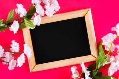 Pembe bir arka plan üzerinde beyaz çiçekler çevrili boş bir kutu ile ahşap bir çerçeve içinde Kara tahta. Uzay kopyalayın. Bahar tatili için şablon.