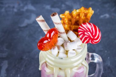 Pembe yüzlü, krem üzerinden Freakshake. Lolipop, waffle ve hatmi ile Monstershake. Bir Mason kavanoza aşırı milkshake. Koyu gri beton arka plan.