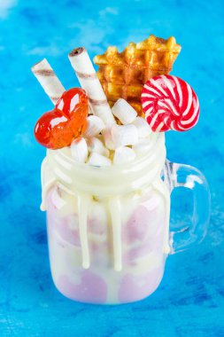 Pembe yüzlü, krem üzerinden Freakshake. Lolipop, waffle ve hatmi ile Monstershake. Bir Mason kavanoza aşırı milkshake. Mavi beton zemin.
