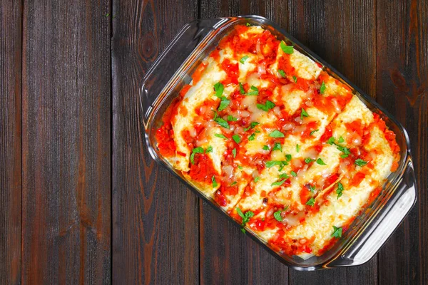 Homemade chicken enchiladas in dish on wooden table. Top view. — Stock Photo, Image