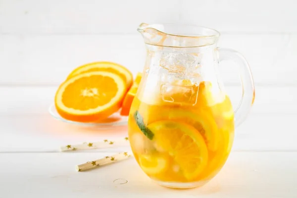 Orangefarbenes Entgiftungswasser in einem Krug auf einem weißen Holztisch. gesunde Lebensmittel, Getränke. — Stockfoto