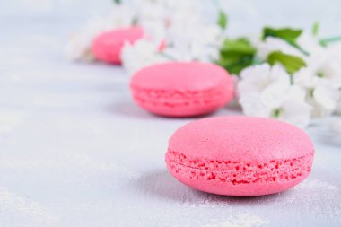Pembe ve mor macaroons pembe ve beyaz çiçekler tarafından çevrili gri bir tablo.