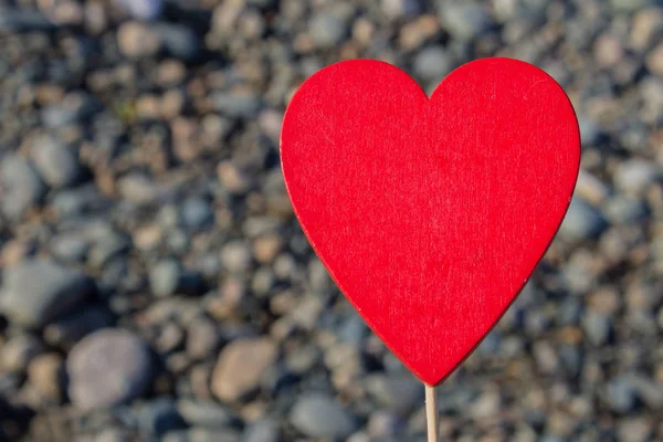 En man innehar ett rött trä hjärta på en pinne mot bakgrund av natur, sky, stenar. Begreppet alla hjärtans dag. — Stockfoto
