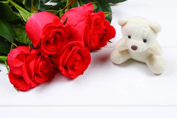 Witte teddybeer omgeven door roze rozen op een witte houten tafel. Sjabloon voor 8 maart, Mother's Day, Valentijnsdag. — Stockfoto