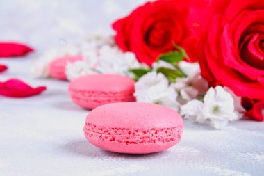 Pembe ve mor macaroons pembe ve beyaz çiçekler tarafından çevrili gri bir tablo.