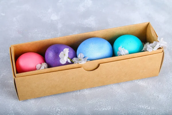 Oeufs de Pâques colorés dans une boîte cadeau sur un fond de béton gris . — Photo