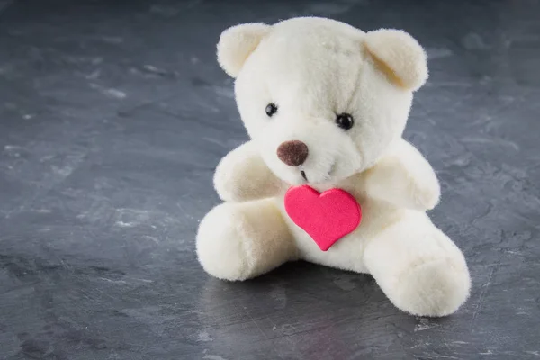 White toy teddy bear with heart on a gray background. The symbol — Stock Photo, Image