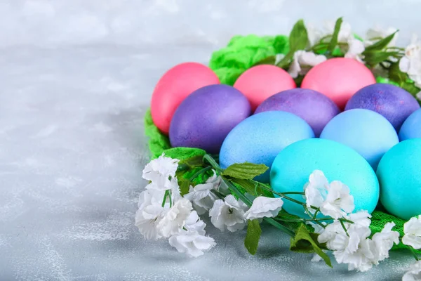 Oeufs de Pâques colorés avec des fleurs blanches sur un fond de béton gris . — Photo