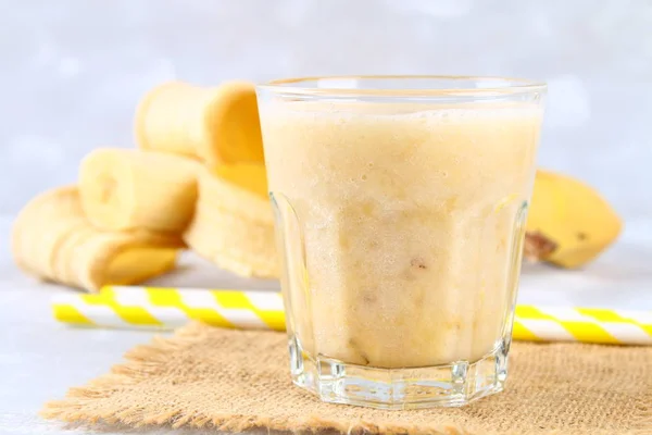 Batido de plátano con tubo de papel y menta. Los plátanos están enteros y cortados sobre un fondo gris . —  Fotos de Stock