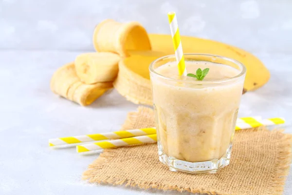 Batido de plátano con tubo de papel y menta. Los plátanos están enteros y cortados sobre un fondo gris . —  Fotos de Stock