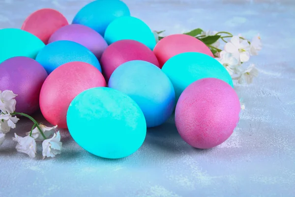 Oeufs de Pâques colorés avec des fleurs blanches sur un fond de béton gris . — Photo