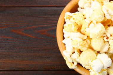 Ahşap bir masa üzerinde ahşap bir kase tuzlu popcorn.