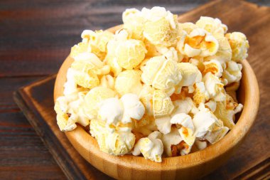 Ahşap bir masa üzerinde ahşap bir kase tuzlu popcorn.