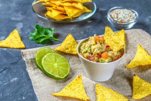 Guacomole is een traditionele Mexicaanse saus uit geraspte avocado, limoensap, rode ui, tomaten, knoflook en chili. Geserveerd met nachos chips. — Stockfoto