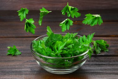 A bowl of parsley with flying leaves on a wooden table. Levitation. clipart