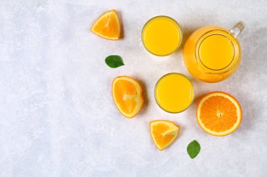 Cam şişeler, gözlükleri ve bir sürahi taze portakal suyu üzerine gri masa lambası turuncu ve sarı renkli boruları dilimleri ile. Üstten Görünüm. Düz Lay.