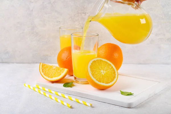 Glass cups and a pitcher of fresh orange juice with slices of orange and yellow tubes on a light gray table. — Stock Photo, Image