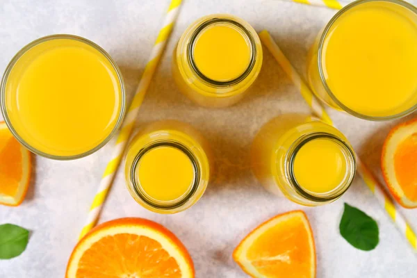 Botellas de vidrio, vasos y una jarra de jugo de naranja fresco con rodajas de tubos de color naranja y amarillo en una mesa de color gris claro. Vista superior. Piso Lay . — Foto de Stock