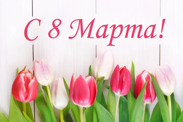 The text in Russian: from 8 March. International Women\'s Day. Tulips on a white wooden table.