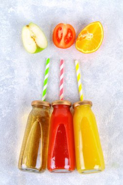 Şişe taze portakal, elma, domates suyu ve renkli tübüllerin bir gri beton tablo ile. Meyve ve sebze çevresinde. Üstten Görünüm. Düz Lay.