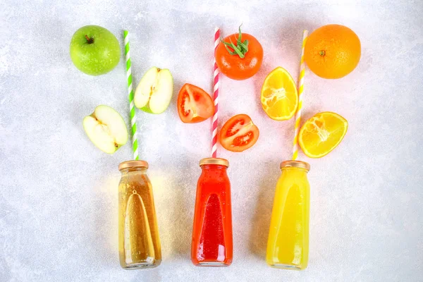 Botellas con naranja fresca, manzana, jugo de tomate y túbulos de colores en una mesa de hormigón gris. Frutas y verduras alrededor. Vista superior. Piso Lay . — Foto de Stock