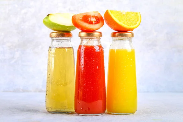 Bottles with fresh orange, apple, tomato juice on a gray concrete table. Lobules Fruits and vegetables around. Top view. Flat Lay. — Stock Photo, Image