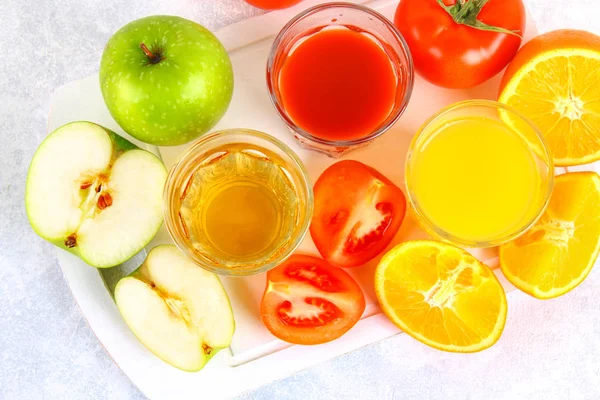 Vasos con naranja fresca, manzana, jugo de tomate sobre una mesa de hormigón gris. Lobulillos Frutas y verduras alrededor. Vista superior . — Foto de Stock