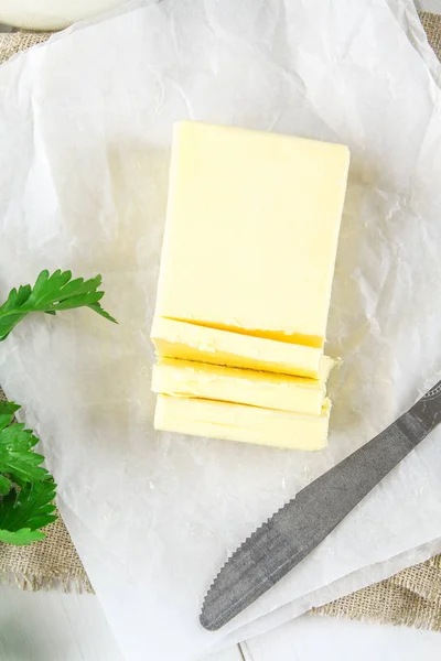 Bar másla je nakrájíme na kousky na dřevěném prkénku s nožem, mléka, vajec a petrželkou na bílém stole. Ingredience pro vaření. — Stock fotografie